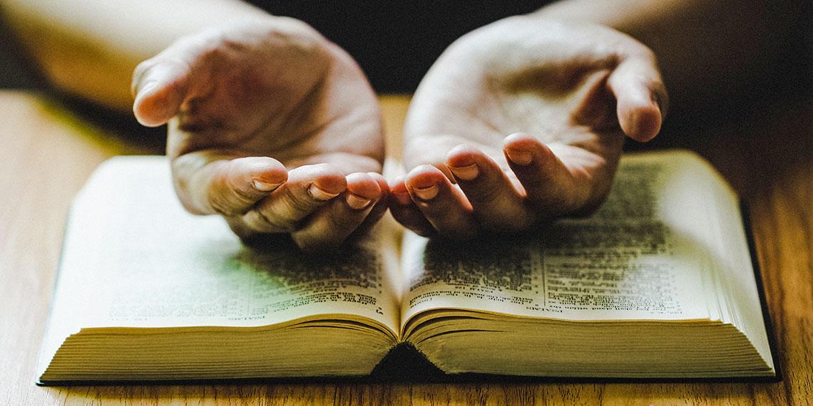 Hands rested in prayer on top of a bible